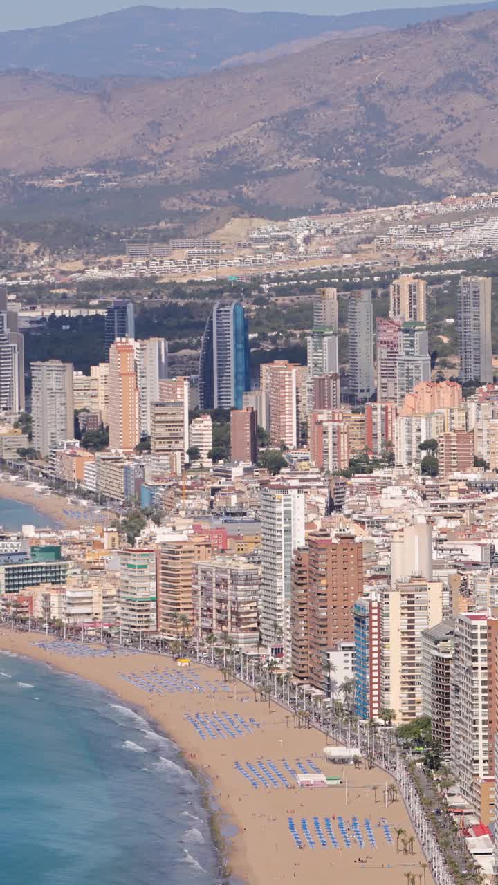 夏季西班牙贝尼多姆镇的肖像镜头显示了莱万特海滩旁的高层公寓和建筑以及背景中的山丘。视频下载