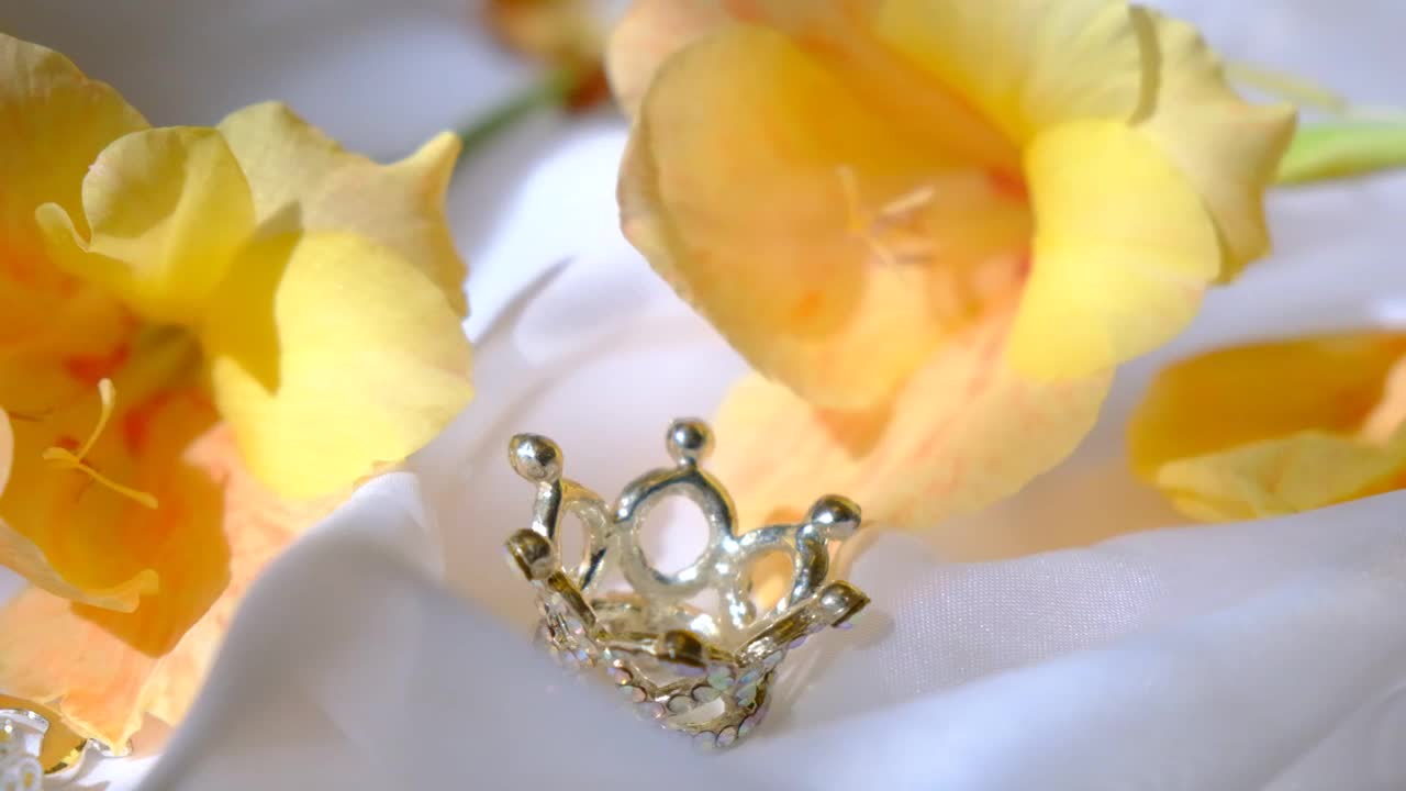 舞会礼服特写。钻石银皇冠，珠宝和黄色的花朵在白色丝绸礼服背景。豪华背景，婚礼，周年纪念，生日，派对，舞会视频下载