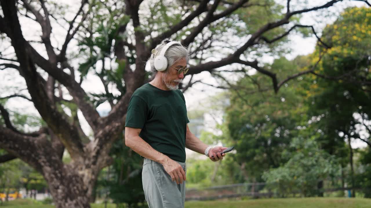 老人在公园散步时使用智能手机。视频下载