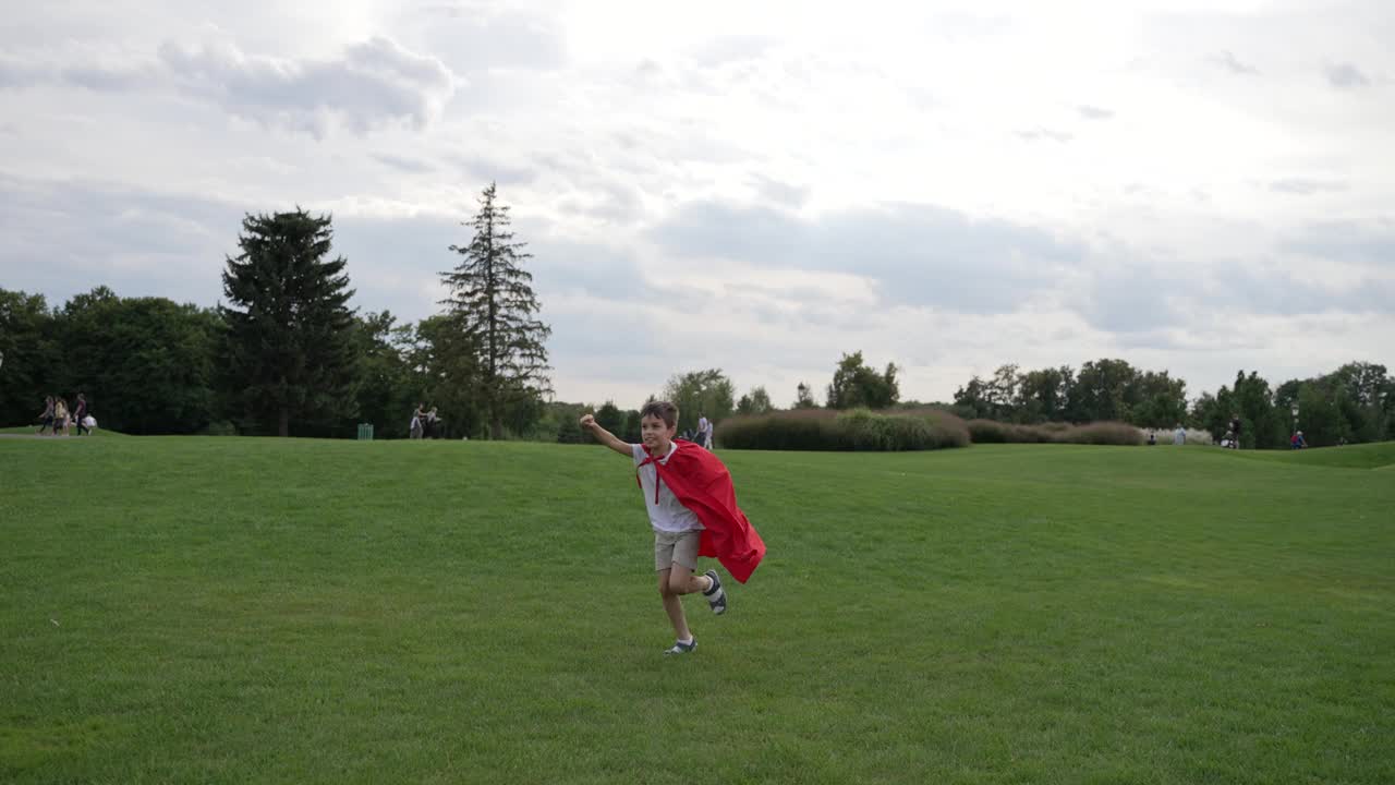 穿着红斗篷的男孩跑过草地视频下载