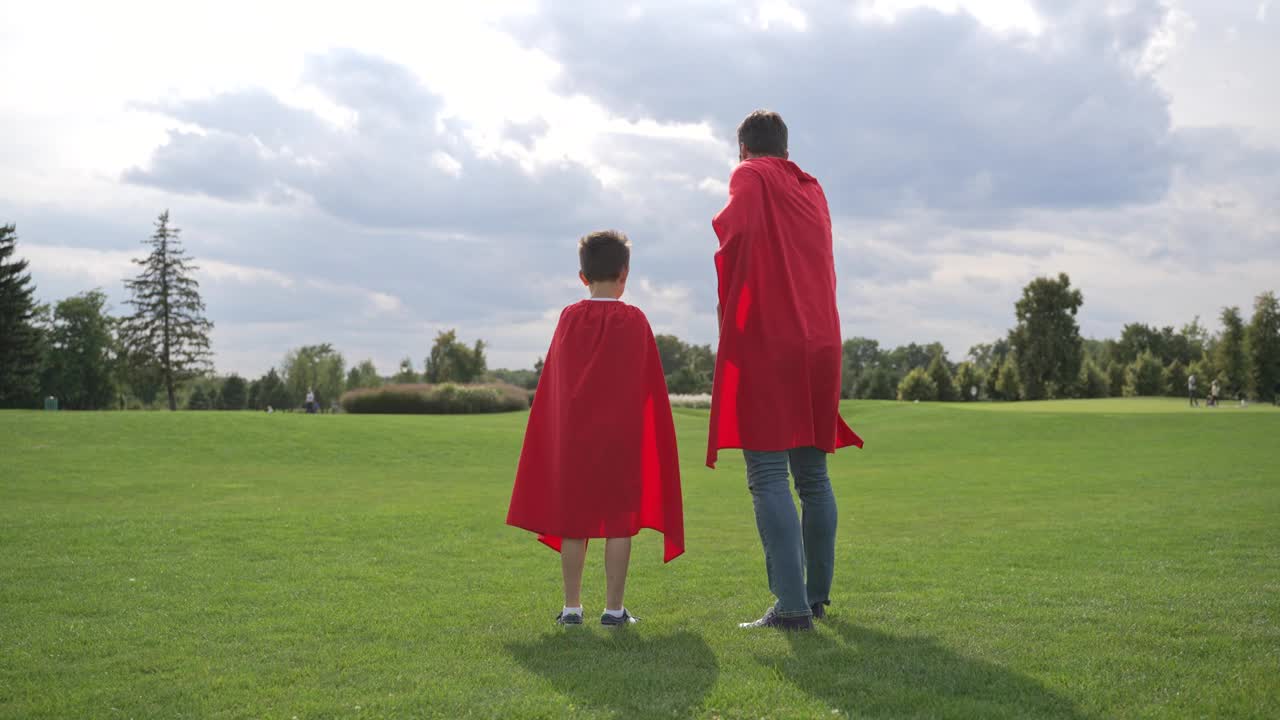 穿着红斗篷的父亲和男孩在草原上奔跑视频下载