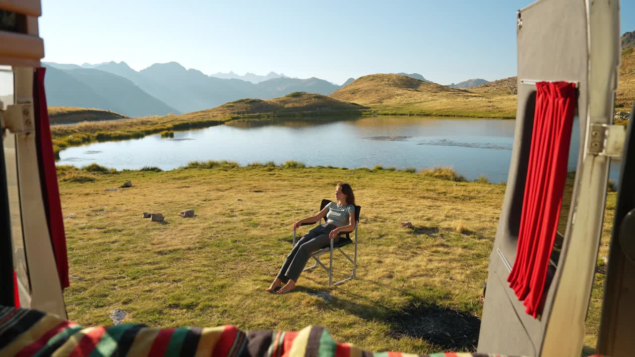一名妇女坐在湖边的折叠椅上，乘坐露营车前往阿尔卑斯山视频下载