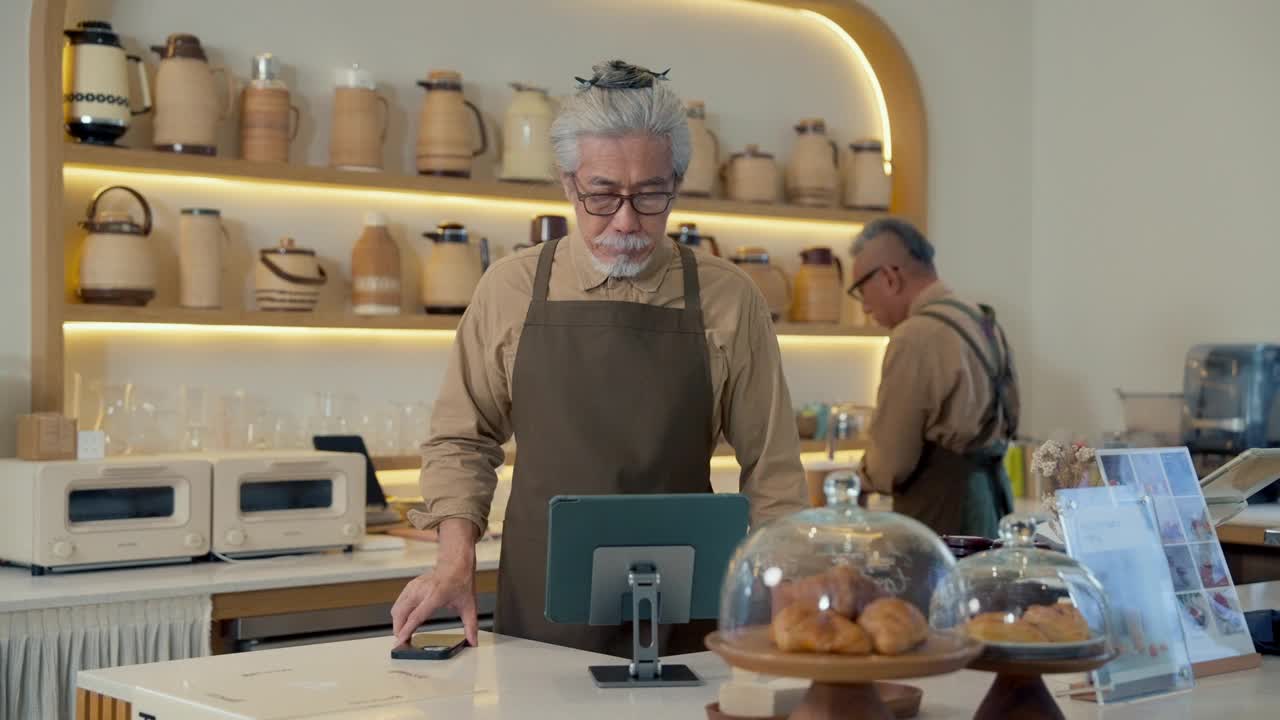 在舒适的咖啡馆里，咖啡店老板正在摆弄平板电脑和会说话的手机视频下载