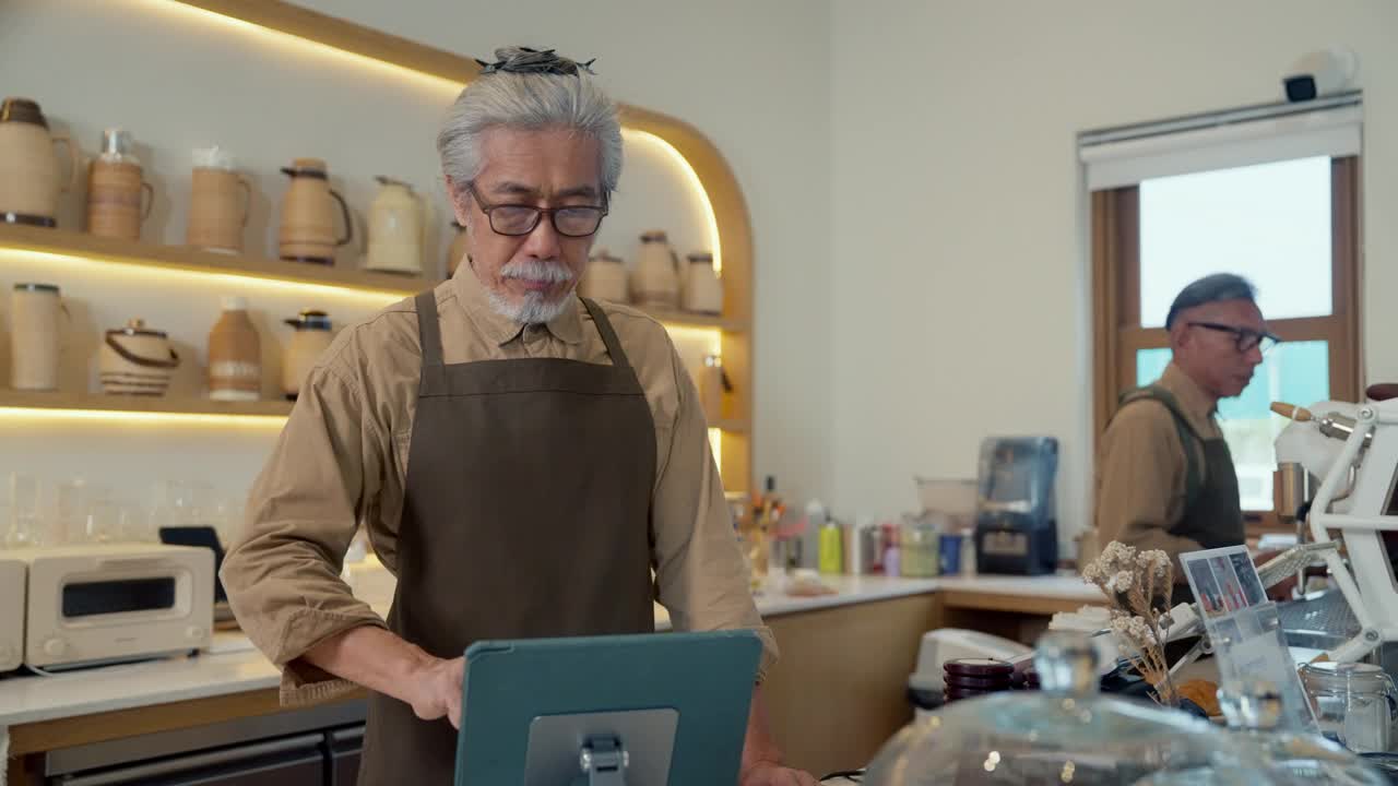 老男人咖啡店老板正在舒适的咖啡馆里制作平板电脑视频下载