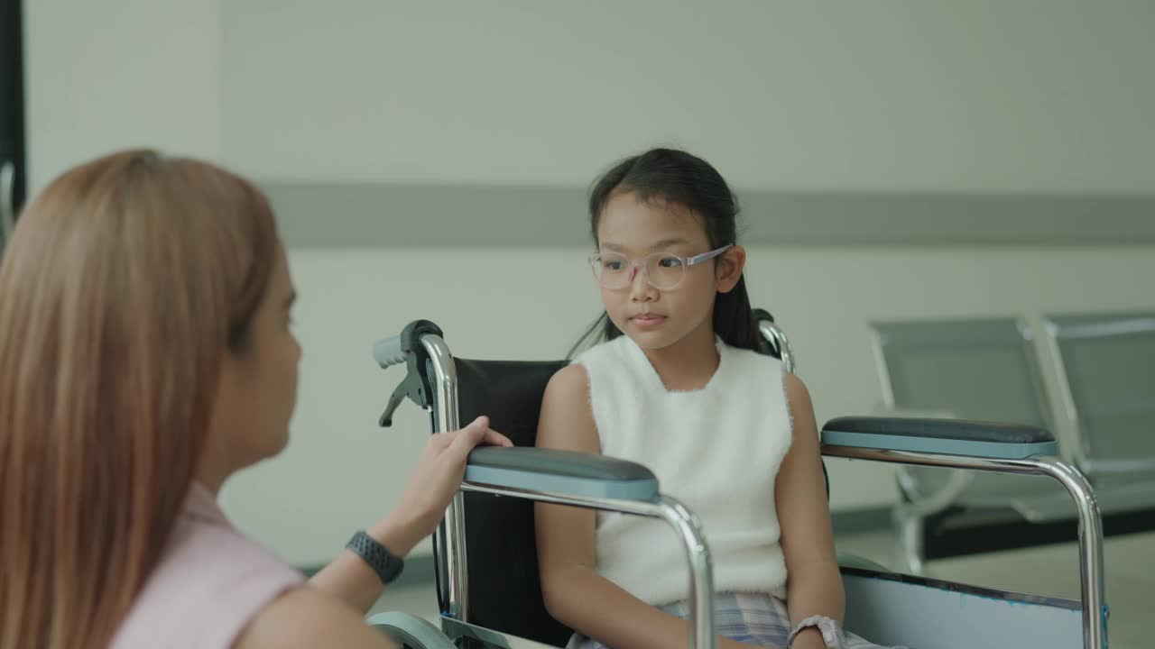 坐在轮椅上微笑的亚洲少女在医院与她的母亲真诚交谈，流露出喜悦和联系。视频下载