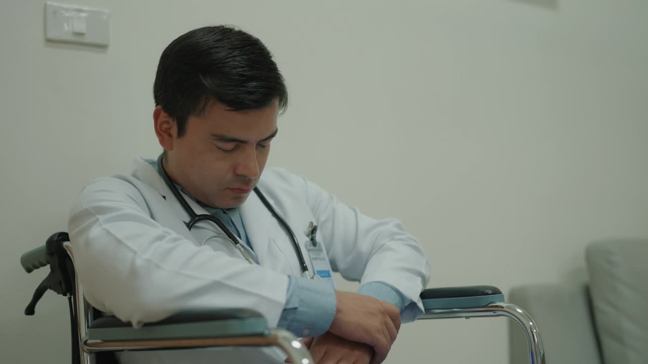 疲惫的医生在医院轮椅上睡觉:长时间轮班后，疲惫的医疗专业人员面临倦怠，体现了临床医护人员的疲劳。视频下载