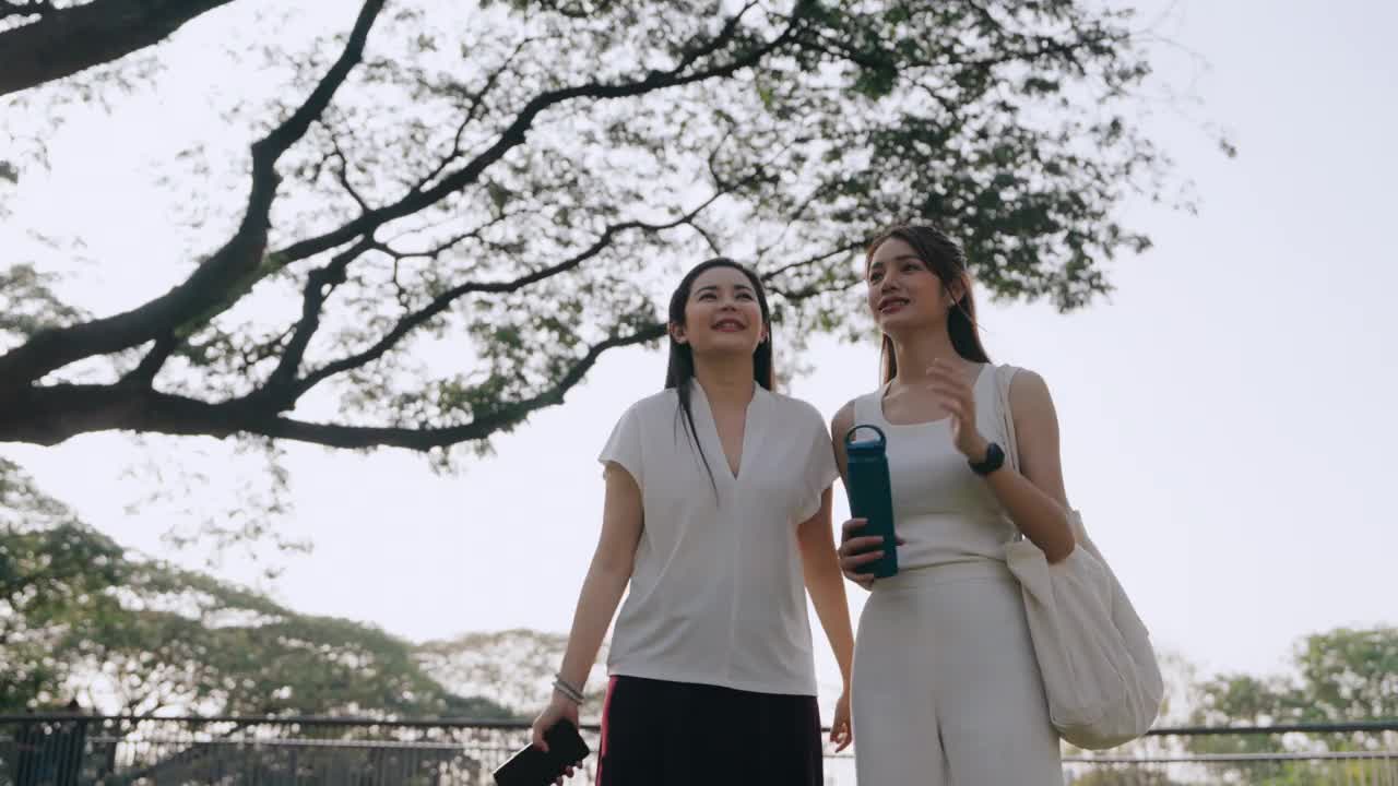 早上在公园散步。两个亚洲女人在阳光明媚的公园里享受清晨的散步视频下载
