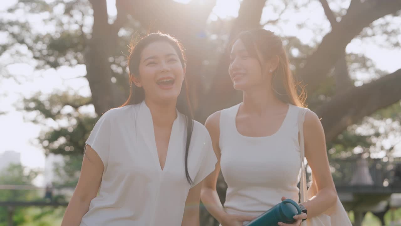 朋友们在公园里欢笑。两个亚洲女人在公园的树下一起笑。视频下载