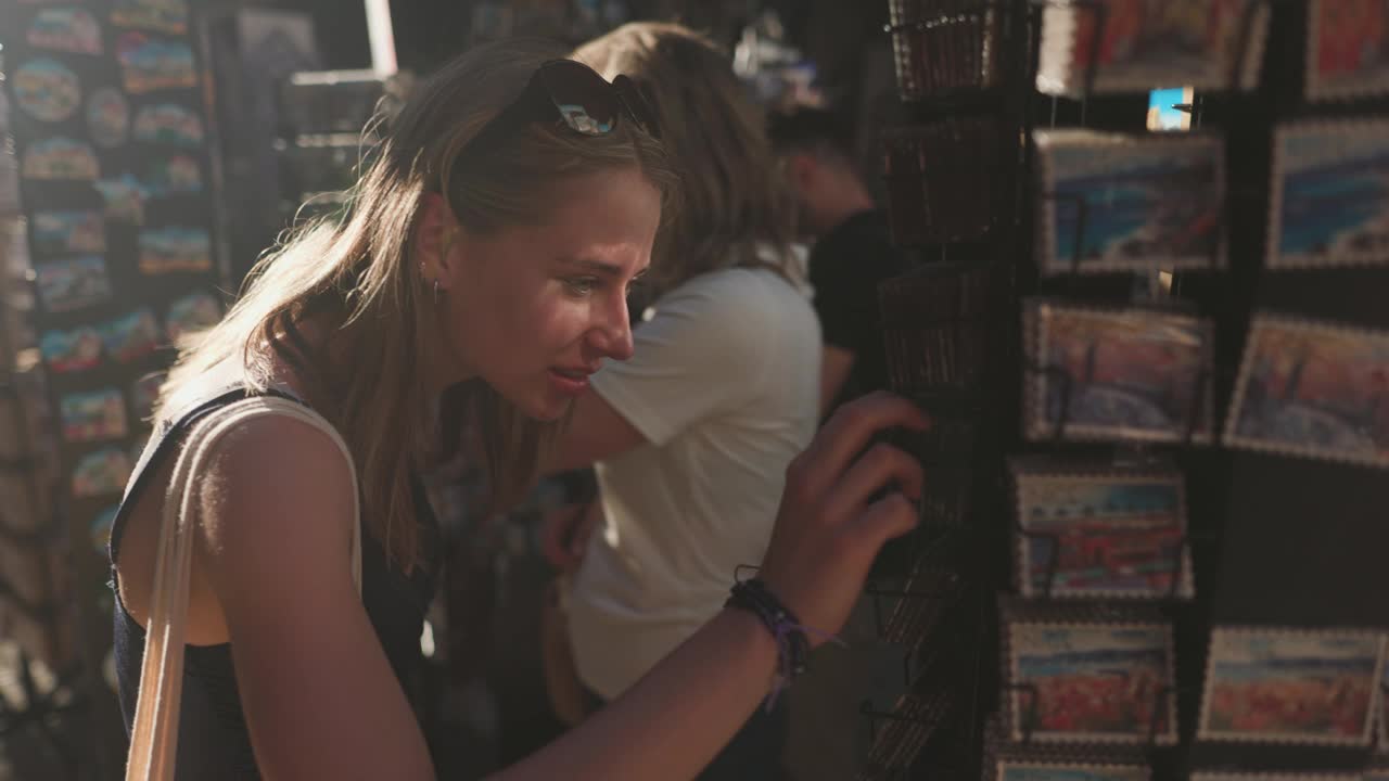 一名年轻女子在法国尼斯老城一家小商店的街头摊位上浏览纪念品贴视频下载