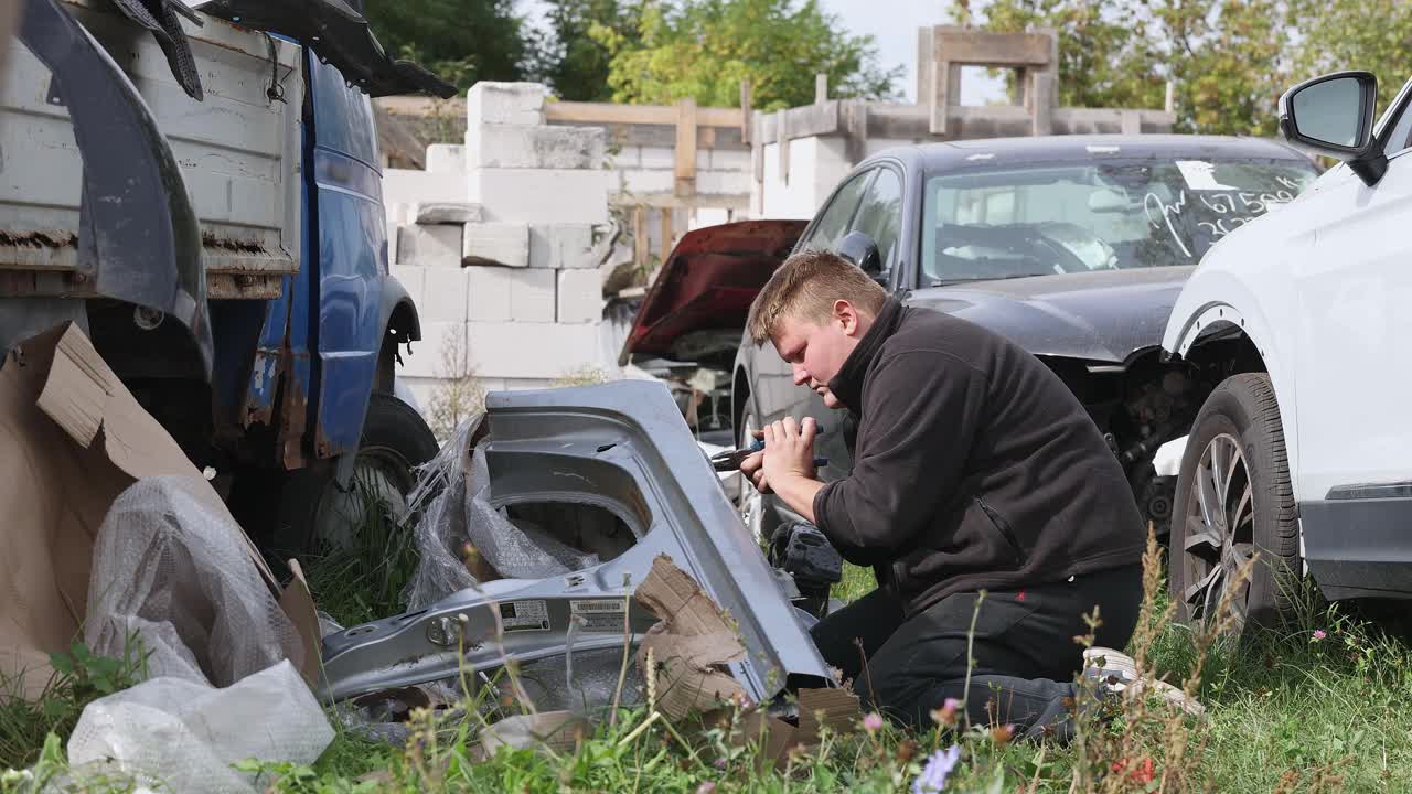 年轻的汽车修理工在一家汽车修理店附近的街道上摆弄汽车的零件。视频下载
