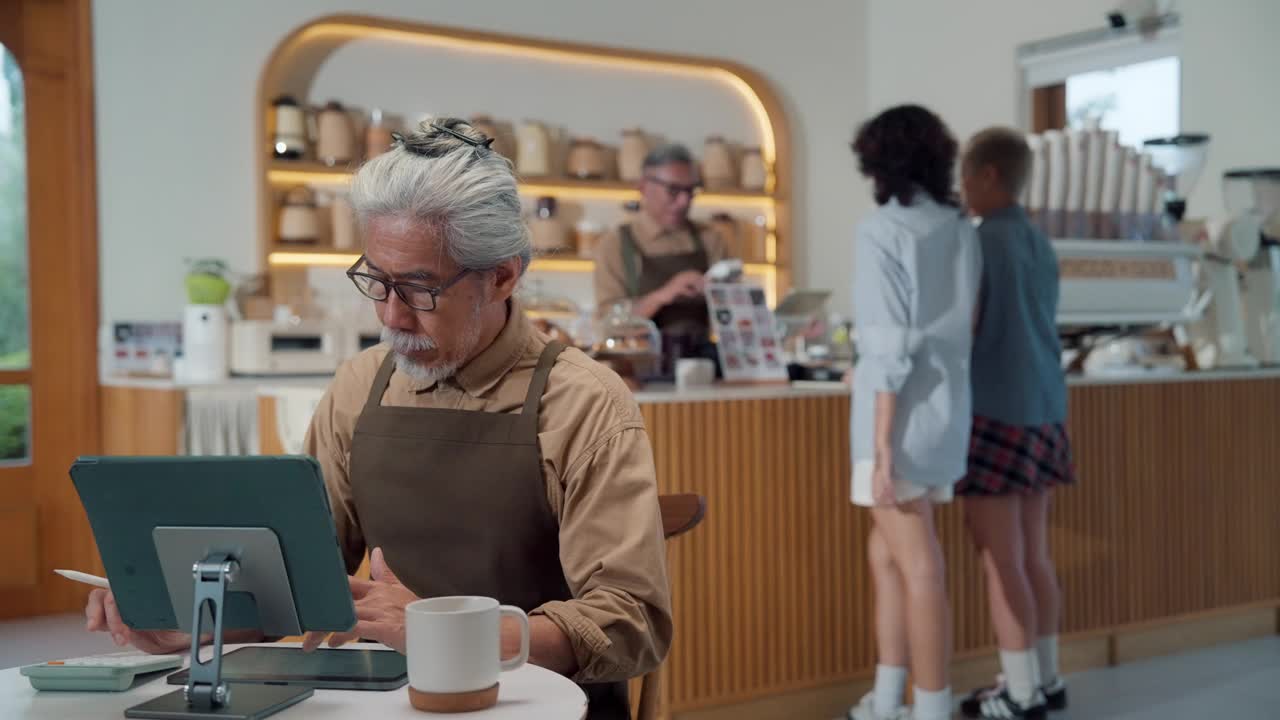 一位年长的咖啡店老板正在咖啡馆里摆弄数码平板电脑。视频下载