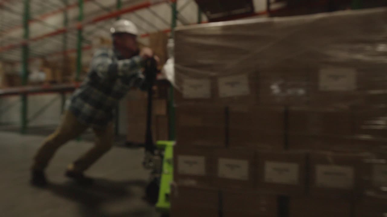 仓库工人用托盘千斤顶推商品的跟踪镜头/美国犹他州美国福克视频下载