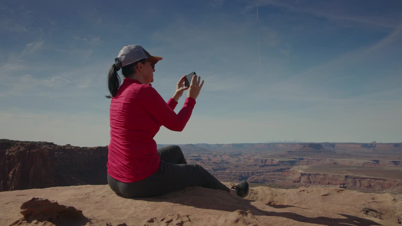 美国犹他州峡谷地国家公园，一名女子坐在俯瞰台上拍摄风景视频下载