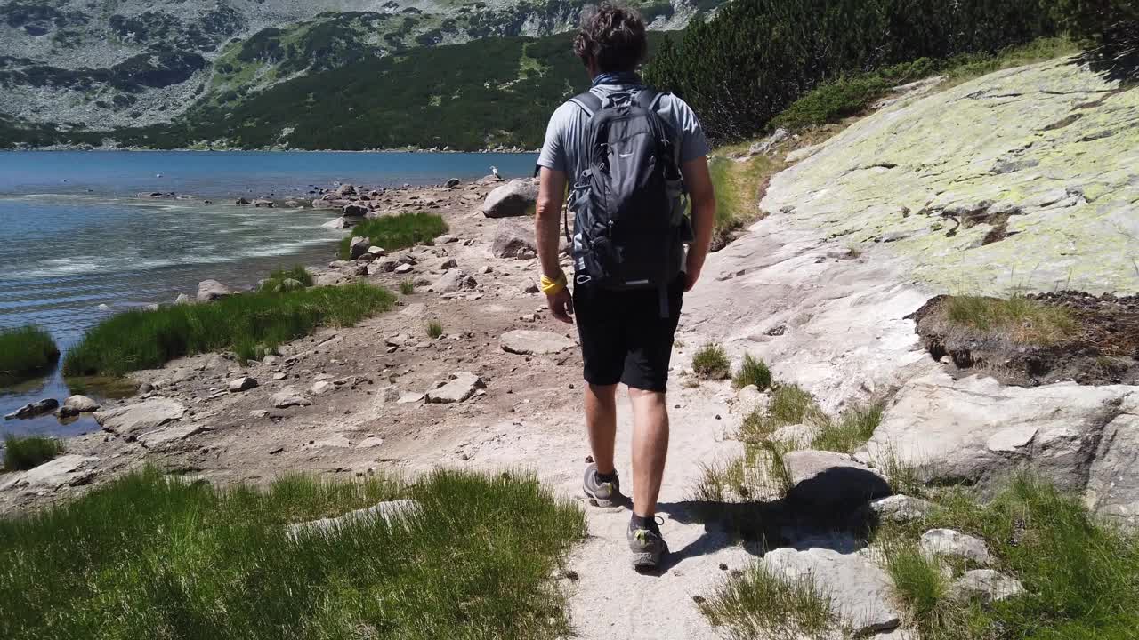 一个孤独的徒步者走在河边的岩石河岸上视频下载