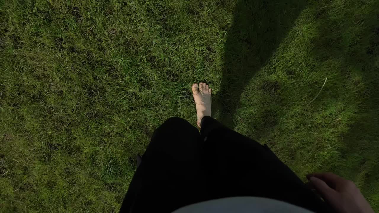 一个女人在阳光明媚的日子里赤脚走在草地上。年轻女子光着腿，赤脚走在草坪上。POV自上而下的视图视频下载