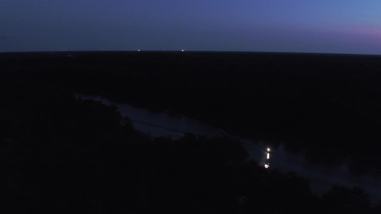 航拍下降镜头照明摩托艇移动在河上在宁静的森林在夜晚- Bayou Vista，德克萨斯州视频下载