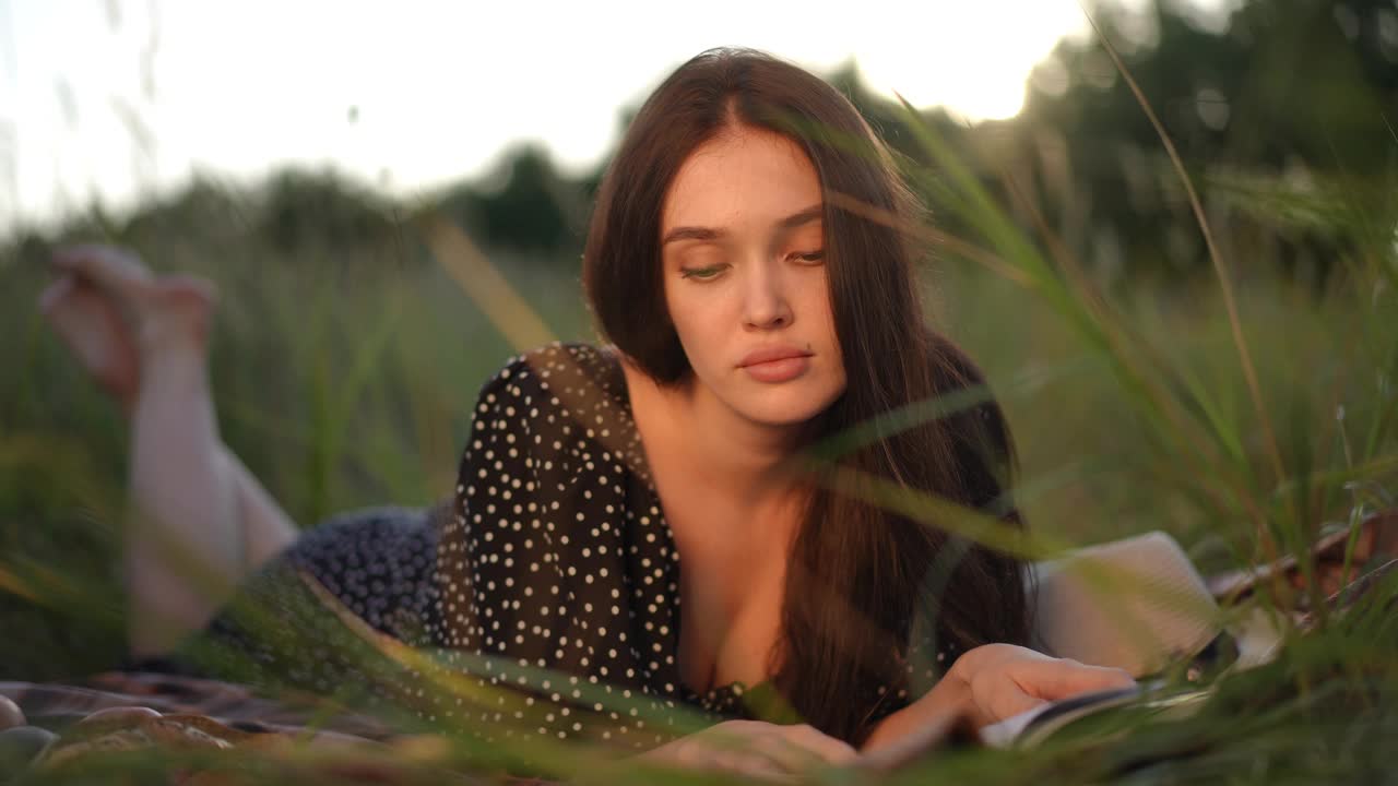 缓慢的运动。一个可爱的女孩喜欢在夏天阳光明媚的日子里躺在草地上看书。视频下载