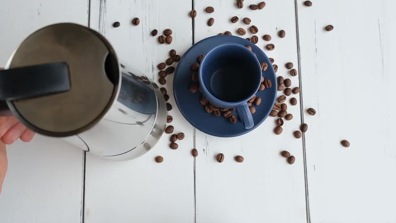 一个男人端着一杯深蓝色的咖啡，在一张白色的木桌上喝着咖啡。视频下载
