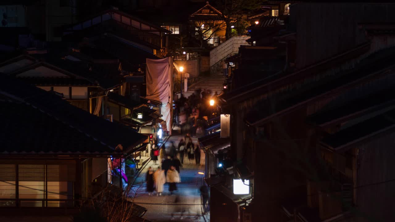 夜间延时拍摄的三内坂街上拥挤的游客步行的视频，街道两旁都是典型的京都联排别墅或町屋建筑视频下载