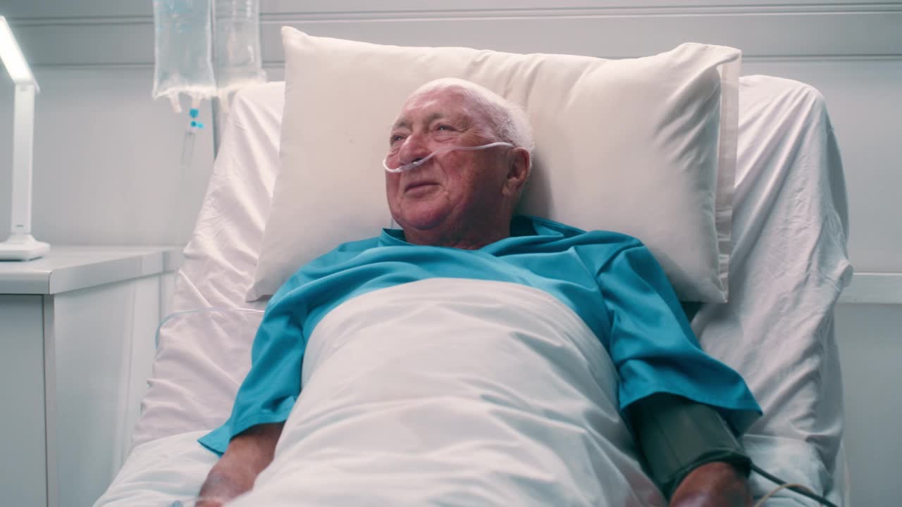 老人躺在病床上，和医生愉快地交谈，讲着有趣的笑话，关心和保健。黑人妇女，护士和病人，笑，喜剧故事或输液的老人在诊所视频下载
