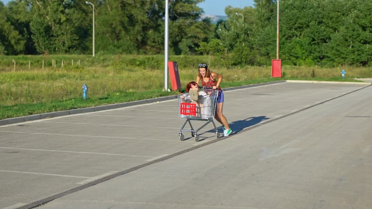两个年轻的女性朋友在停车场的购物车里玩耍视频下载