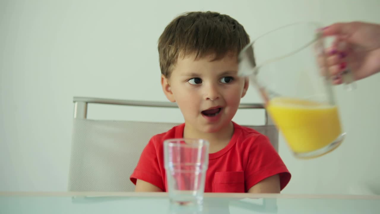 当橙汁被倒进杯子时，男孩饶有兴趣地看着视频下载