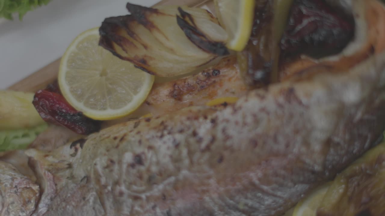 餐桌上木质盘子里的烤鱼和蔬菜的俯视图，背景模糊视频下载