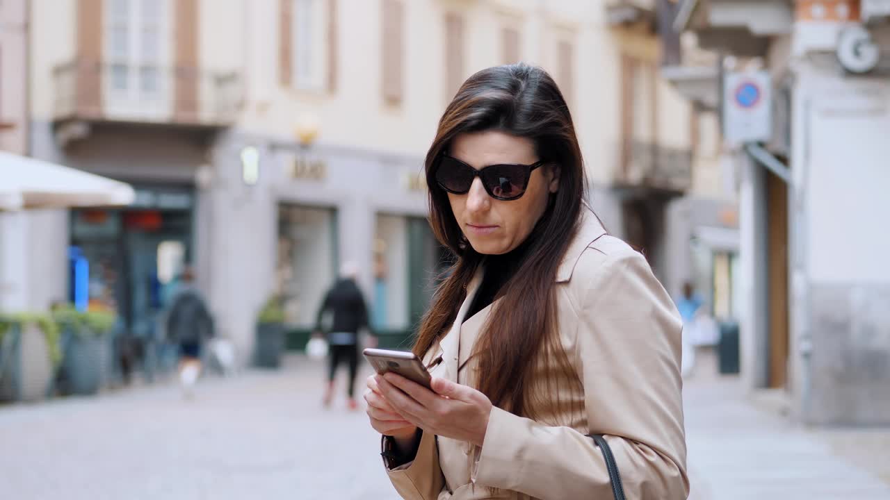 一名女商人在欧洲城市散步时玩着智能手机视频下载
