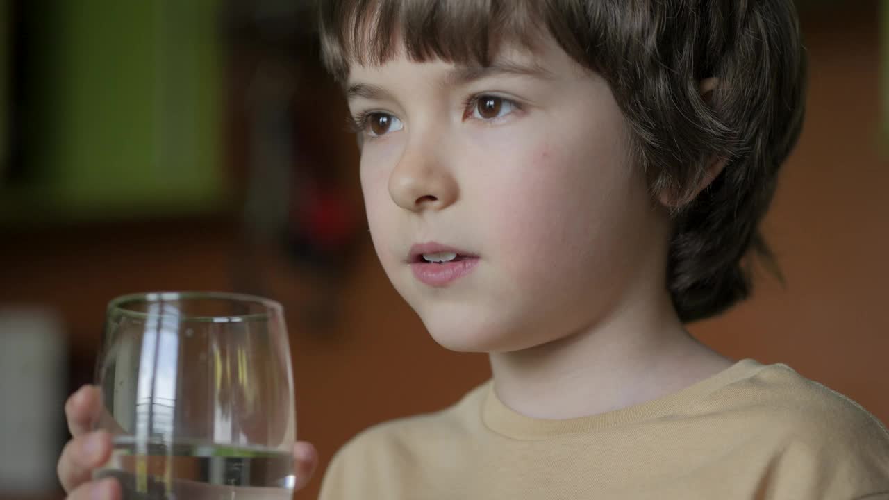 男孩从杯子里喝干净的水。小男孩在家里喝玻璃新鲜透明纯过滤矿泉水。特写孩子喝杯水健康的身体护理。健康的生活方式。视频下载