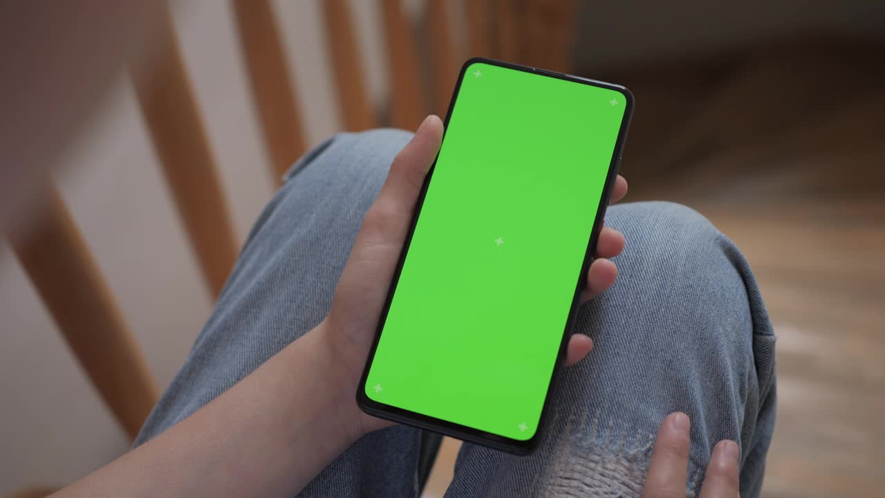 女孩拿着绿屏的智能手机坐在家里的楼梯上。妇女使用手机绿屏模拟色度键。孩子看视频，社交媒体，玩电子游戏。视频下载