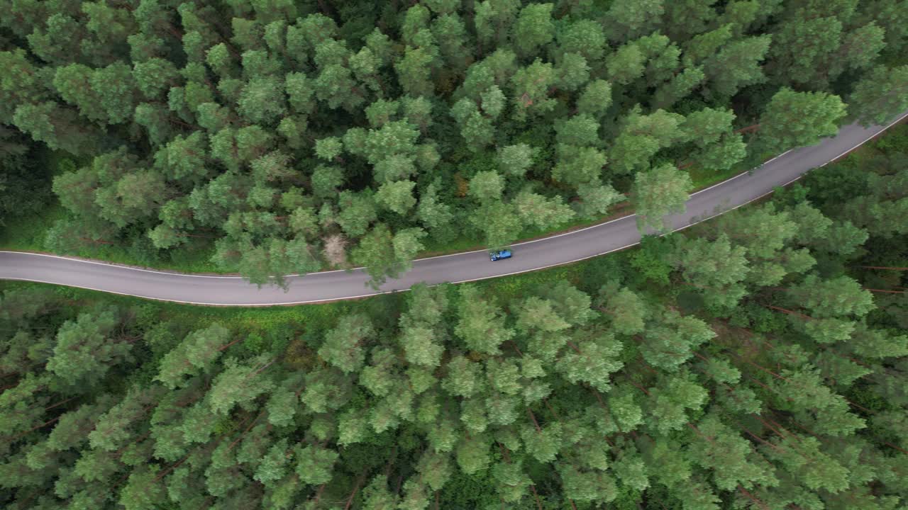 夏日，蓝色汽车行驶在柏油路上，穿过广阔的森林。汽车在松林道路上行驶的航拍照片。穿越森林的公路旅行。风景优美的夏季景观。视频下载