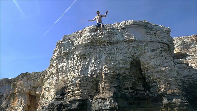 慢镜头:一名男子从海边的悬崖上跳下视频下载