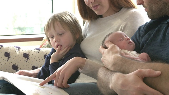 一家人坐在沙发上，新生儿在看书视频素材
