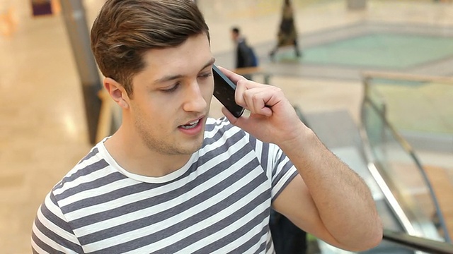 一名年轻人在手机上乘坐购物中心的自动扶梯视频素材