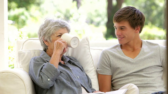 老奶奶坐着看书，孙子拿来了热饮视频素材