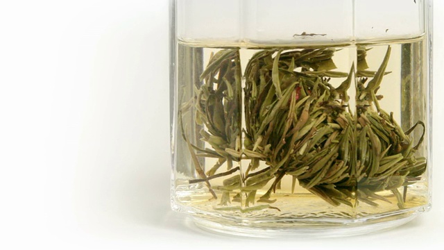 绿色的中国花茶是冲泡和溶解在玻璃上面的白色背景。延时视频视频下载