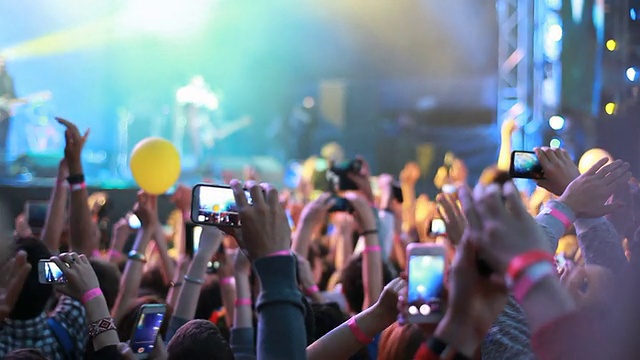 歌迷们在音乐会上挥舞着他们的手，拿着带有数字显示器的手机。视频下载