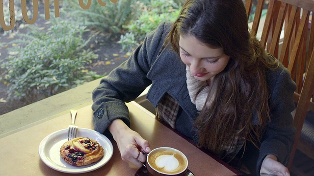 一个年轻的女人独自坐在咖啡店的一张桌子旁，喝着一杯咖啡视频素材