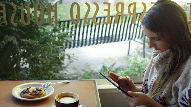一个年轻的女人坐在咖啡馆的一张桌子旁，一边喝着咖啡，一边看着窗外视频素材