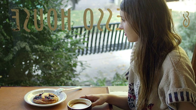 一个年轻的女人独自坐在咖啡店的一张桌子旁，一边喝着咖啡，一边看着窗外视频素材