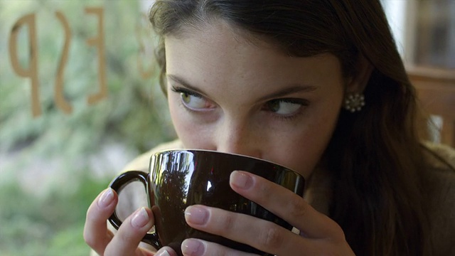 一个年轻的女人在咖啡馆喝咖啡的特写视频素材