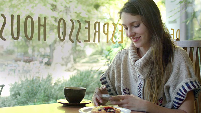 一个年轻女子坐在咖啡馆里，一边喝着咖啡，一边发短信视频素材