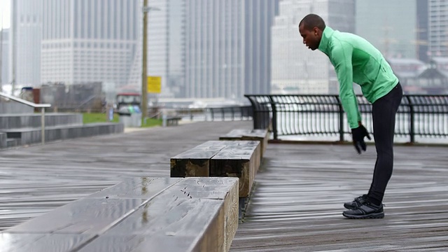 在布鲁克林的桥旁边，一名男子在跑步前伸展身体视频素材