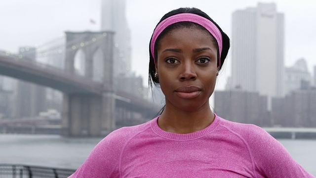 一个女人在一个阴天，在布鲁克林大桥前的跑步装备看镜头的特写视频下载