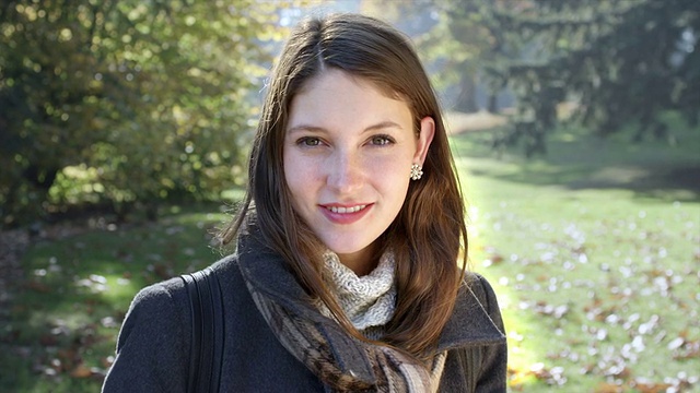 一位年轻女子站在公园里，对着镜头微笑视频素材