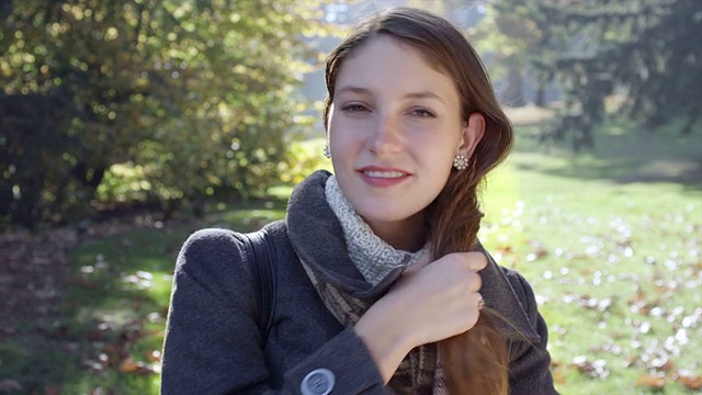 一位年轻女子站在公园里，对着镜头微笑视频素材