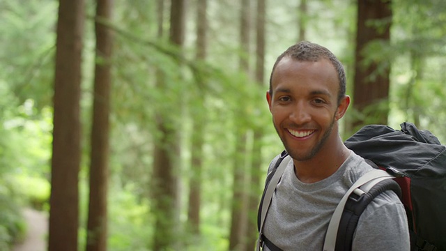 一名徒步旅行者望向树林，然后对着镜头微笑视频下载