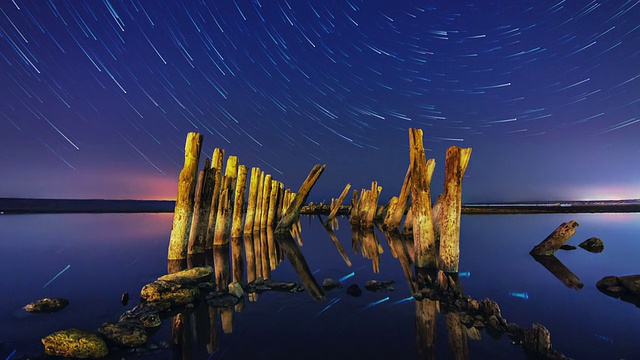 一颗星星在夜晚的轨迹与木柱和浅水在前景的时间流逝视频下载