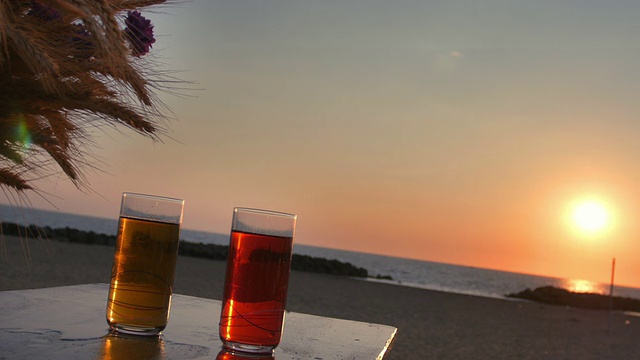 海滩边的桌子上放着两杯鸡尾酒:夏天，日落，喝酒视频素材