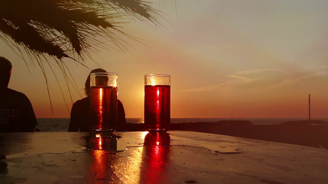 夕阳下，一对情侣在海边喝着鸡尾酒:夏天，爱情，假期视频下载